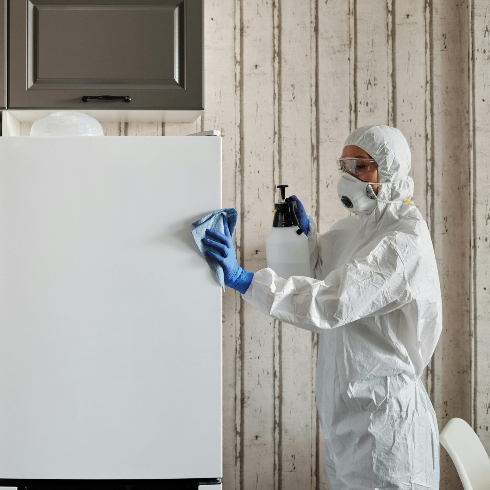A person in protective gear cleaning a kitchen appliance to ensure hygiene.
